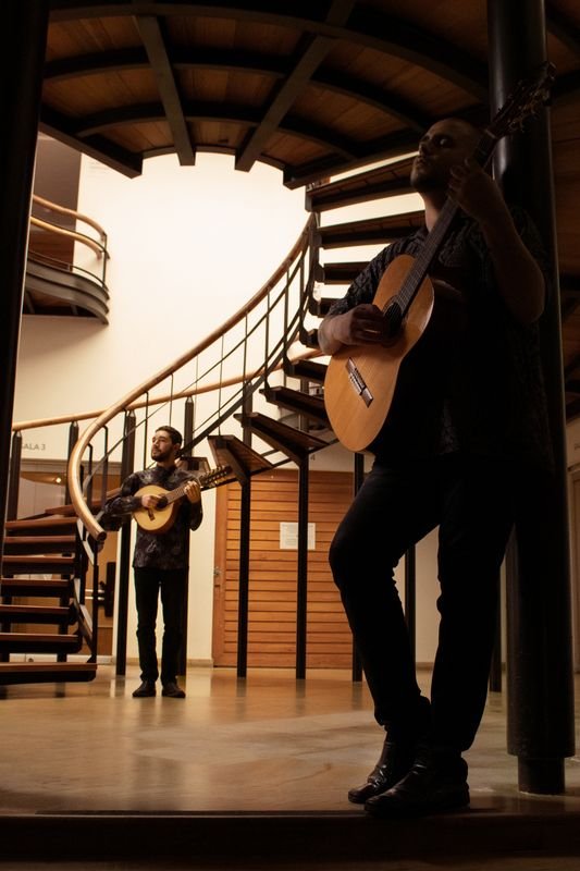 David Valencia con la guitarra bajo una escalera de caracol y Brayan Ruiz al fondo con la bandola