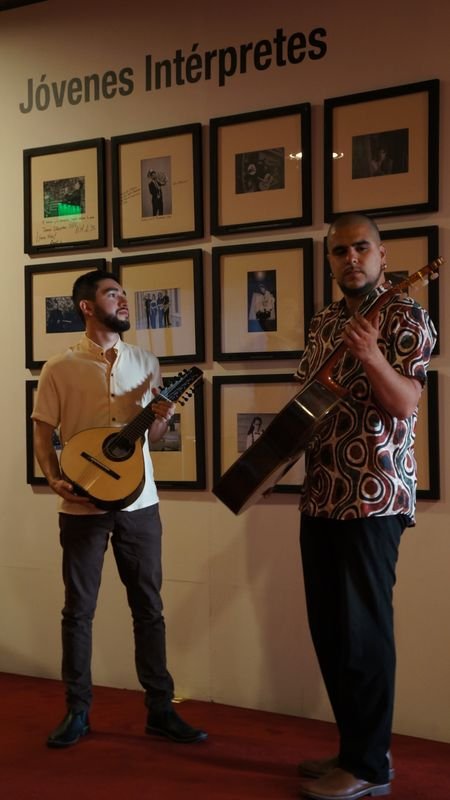 Brayan Ruiz y David Valencia con sus instrumentos frente al muro de fotografías de Jóvenes Intérpretes